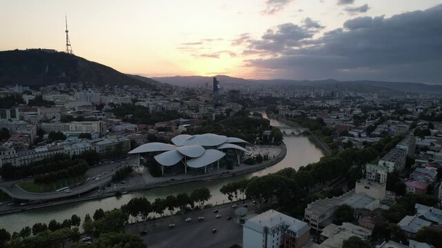 Aerial view of city center in Tbilisi at dusk, flying above the Mtkvari Kura River. Warm sunset light and calm evening atmosphere. High-quality 4K footage.