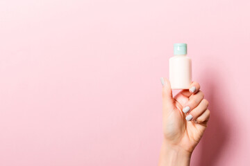 Female hand holding cream bottle of lotion isolated. Girl give tube cosmetic products on pink...