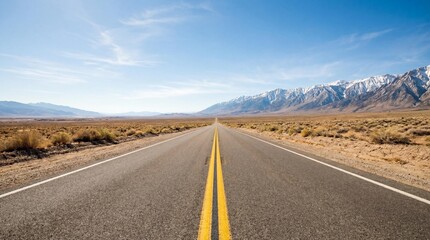 Fototapeta premium A long, straight asphalt highway stretching into the distance through a vast arid desert landscape, with bold yellow center lines leading toward distant snow-capped mountains.