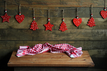 Christmas background with garland of red heart-shaped toys, Christmas trees and stars and wooden table with checkered towel. New Year's mockup