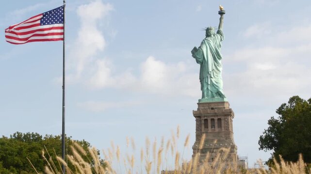 Statue of Liberty on Liberty Island, New York, United States. Cooper monument from behind, democracy and patriotism symbol near Manhattan, NYC USA. American flag waving in wind. Independence concept.