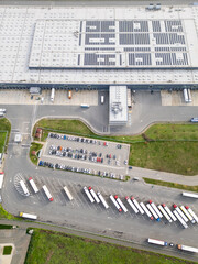 Aerial view of a large logistics warehouse with loading docks and trucks, distribution center surrounded by farmland. Supply chain and transportation concept