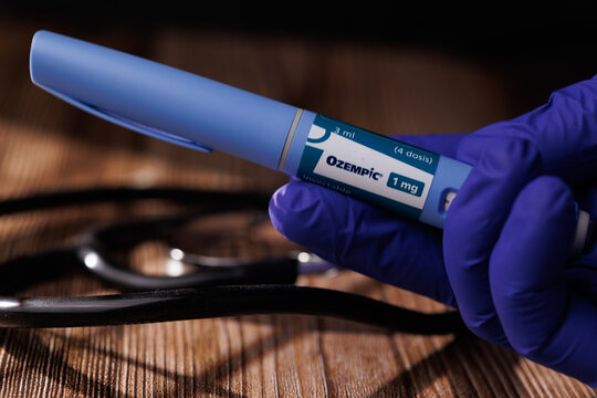 Close up of a blue gloved hand with Ozempic semaglutide pen and stethoscope on dark wood for diabetes and weight management concepts. In Barcelona - Spain, December 22, 2025