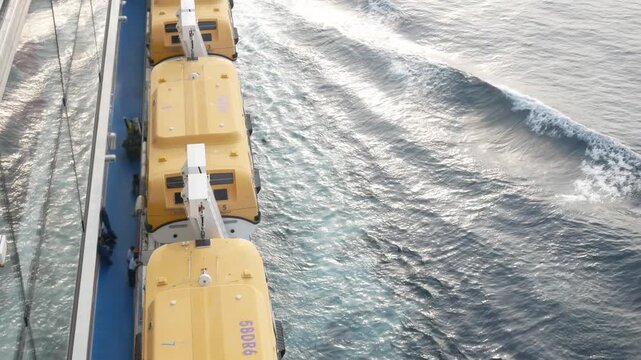 Lifeboat on giant cruise ship view down to ocean surface with waves below while ship cruising saling in the sea. safety muster lifeboat equipment. Holiday vacation summer background