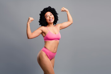 Young woman in pink bikini flexing arms smiling in studio fitness and body positivity portrait