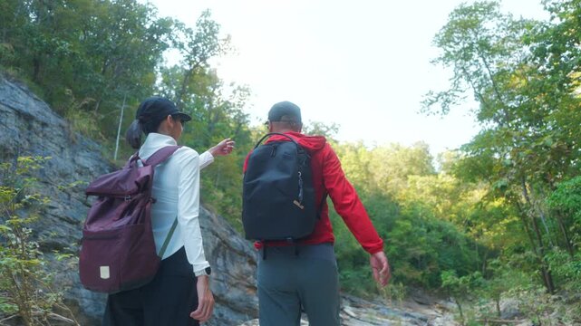 Two asian hiker stands on a light colored rock beside a gentle flowing stream are enjoy their hiking trip is look very happy to have reached their destination.