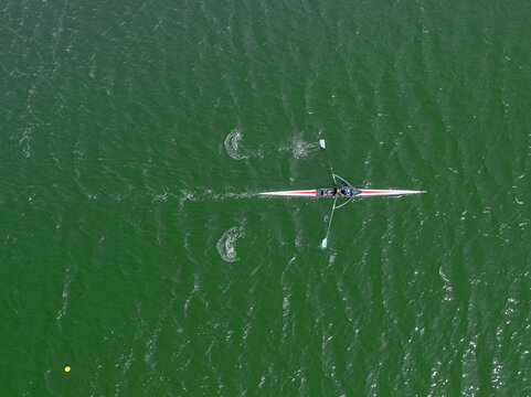 Aerial view of a lone rower cutting through the emerald-green waters with rhythmic strokes, creating a mesmerizing dance of motion, Ciudad de la Costa, Departamento de Canelones, Uruguay.