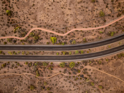 Aerial view of a highway cutting through the arid landscape, with winding trails snaking across the rust-colored earth, and punctuated by scattered greenery, Phoenix, Arizona, United States.
