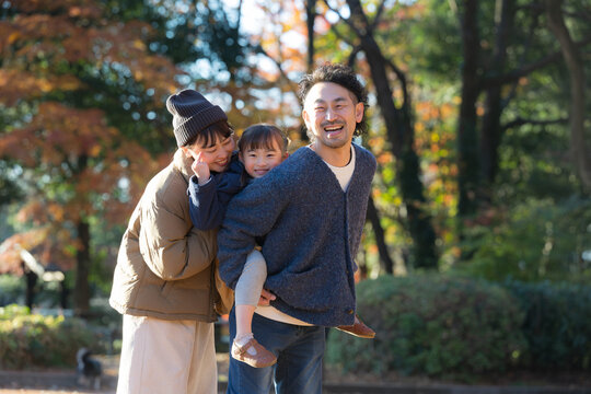 秋の公園で遊ぶ家族 お出かけやレジャーのイメージ　おんぶで仲良しファミリー