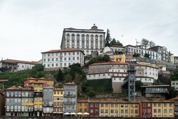 Fototapeta premium Vista panorâmica da encosta histórica do Porto a partir de Gaia. O contraste entre o casario colorido da Ribeira, o funicular dos Guindais e a imponência do Paço Episcopal sob um Céu nublado