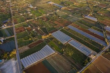 Aerial view of a patchwork of agricultural fields and greenhouses, stitched together by narrow roads under the warm glow of the setting sun, Mellieha Bay, Malta.