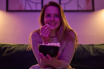 Female seated indoors eating popcorn and watching screen