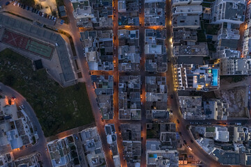 Aerial view of a grid-like pattern of glowing streets cutting through dense buildings, creating a captivating urban tapestry, Mellieha, Malta.