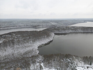 Aerial view of frozen lakes reflecting the overcast sky, fringed by forests dusted with snow, creating a serene winter landscape, Bestensee, Brandenburg, Germany.