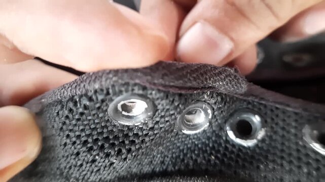 Close up of male fingers threading a black shoelace into a metal eyelet on a black canvas sneaker shoe