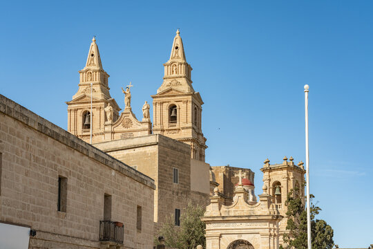 View of the Mellieha Parish Church stands tall against a vibrant blue sky, its intricate stonework and twin bell towers a testament to Maltese architecture, Mellieha, Malta.