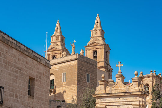 View of the Mellieha Parish Church towers rise against a clear blue sky, showcasing intricate stonework and architectural details, Mellieha, Malta.