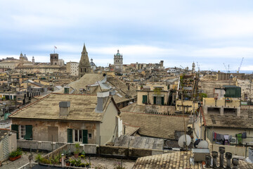 View of weathered rooftops and ancient spires pierce the skyline under a soft sky, creating a timeless vista of urban charm, Genoa, Liguria, Italy.