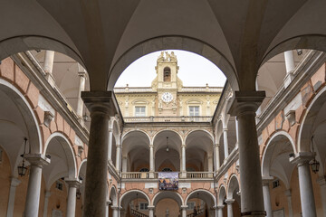 View of intricate arches framing Strada Nuova Museums - Palazzo Rosso with a clock tower, creating a layered perspective in the heart of Genoa, Liguria, Italy.