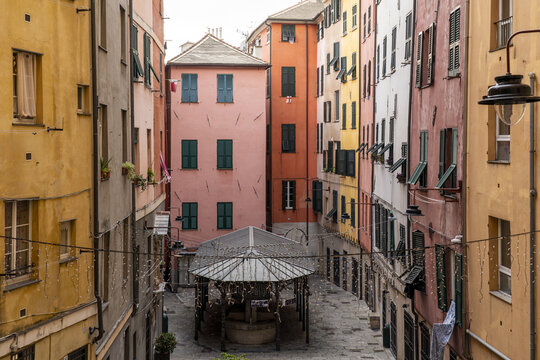 View of colorful buildings casting shadows on cobblestone streets, a charming well nestled amidst the architecture, creating a vibrant European scene, Genoa, Liguria, Italy. - Powered by Adobe