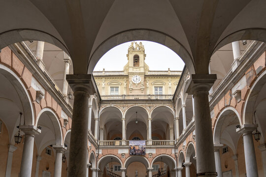 View of intricate arches framing Strada Nuova Museums - Palazzo Rosso with a clock tower, creating a layered perspective in the heart of Genoa, Liguria, Italy.
