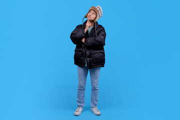 Full body of thoughtful young Asian man wearing winter clothing against blue background
