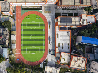 Aerial view of the vibrant green sports field sharply contrasts against the orange running track and building roofs, creating a striking geometric pattern, Changsha, Hunan, China.