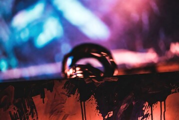 Abstract vibrant neon lights illuminate a blurry metallic object and textured foreground, creating a mysterious and energetic atmosphere.