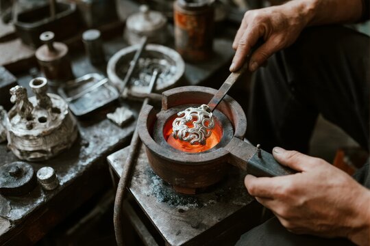 Artisan heating a metal object in a forge using tongs and a crucible - Powered by Adobe