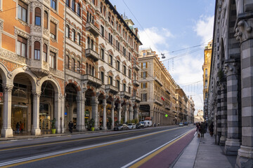 Genoa, Italy - 27 December 2022: View of Via Roma, where ornate facades in warm hues meet the cool shadows, as pedestrians traverse the elegant street.
