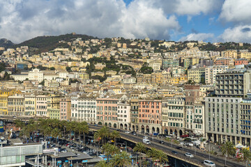 Genoa, Italy - 27 December 2022: View of the colorful facades of buildings lining the harbor, cascading up the hillside under a bright sky.