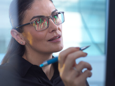 Financial analyst observing market data on computer with graph reflection