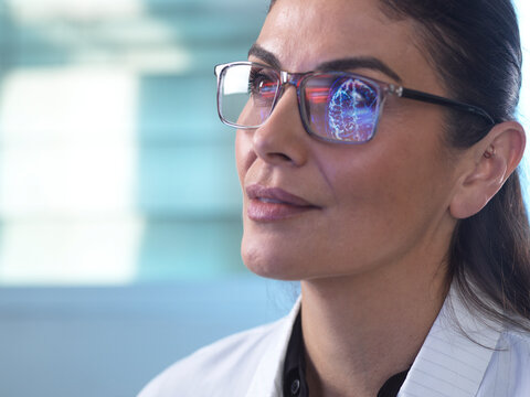 Doctor analysing brain scan with digital reflection in glasses