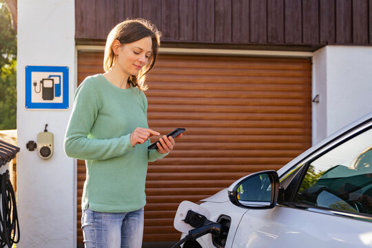 Woman using mobile app to charge electric car at home charging station