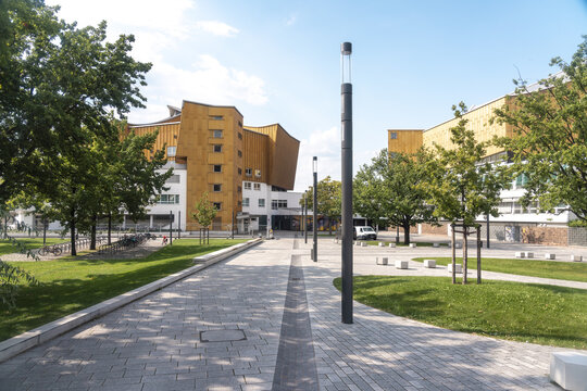 Berlin, Germany - 27 August 2019: View of the Philharmonie's golden facade against a backdrop of verdant trees and clear skies, framed by the geometric patterns of the walkway below.