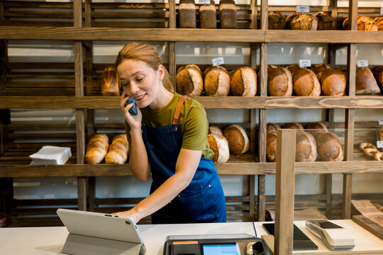 Smiling bakery owner taking order on mobile and using digital tablet