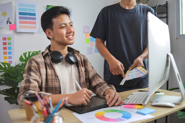 Two Young Asian Male Designers Working Together, Discussing Color Choices With Swatch Fan