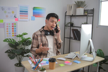 Young Asian Graphic Designer Discusses Work on Phone Call at His Modern, Bright Home Office Desk