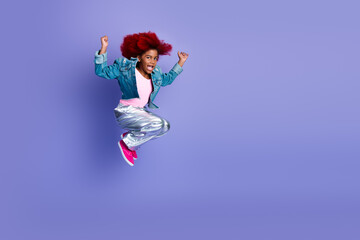 Young girl jumping in the air wearing a denim jacket pink shirt metallic pants against a purple background