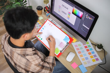 Young Asian Graphic Designer Actively Sketching Logo Concept on Paper Using Colored Pencils