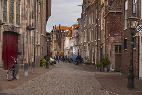 Leiden, Netherlands - 05 May 2019: View of the cobblestone street leading towards the Garenmarkt, lined with aged brick buildings and punctuated by the dark red door of an ancient church.