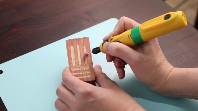 Woman engraving a wooden block with a ceramic tip hand tool, creating decorative patterns for craft or art.