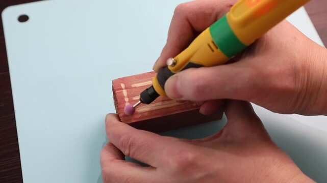 Woman uses a hand engraving tool with a ceramic tip to engrave on a painted wooden block. Crafting and diy hobby concept.