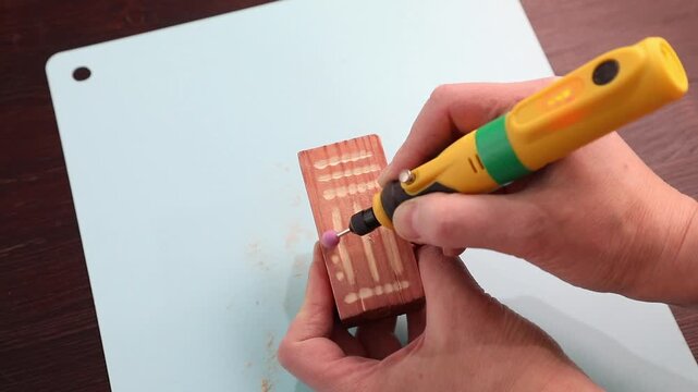 Woman using a hand engraving tool with a ceramic tip to carefully engrave patterns on a painted wooden block. Crafting and diy home decor art.