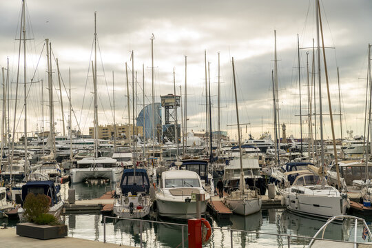 Barcelona, Spain - 07 November 2016: View of the harbor filled with white yachts and boats, their masts reaching high against the backdrop of the W Barcelona hotel.