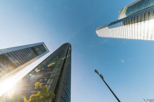 Madrid, Spain - 10 November 2016: View of Cuatro Torres Business Area skyscrapers piercing the vivid blue sky, sunlight glinting off the glass and steel, modern architecture reaching for the heavens.