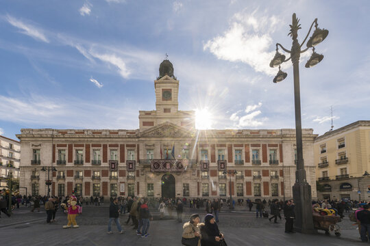Madrid, Spain - 09 November 2016: View of the iconic Casa de Correos basking in the sun, with the bustling Puerta del Sol alive with people under a bright sky.