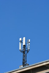 A telecommunication antenna tower with multiple transmitters stands against a clear blue sky on top of a city building
