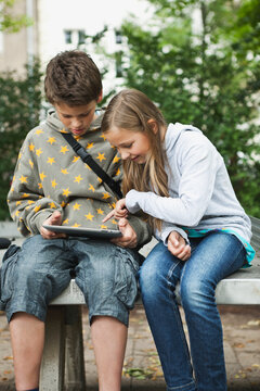 Children using tablet outdoors on park bench in Berlin in summer