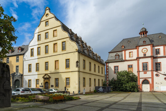 Koblenz, Germany - 16 September 2025: View of Alter Kaufhaus's pale yellow facade glowing softly under a sky streaked with clouds, contrasting with the darker roof of the Altes Rathaus.